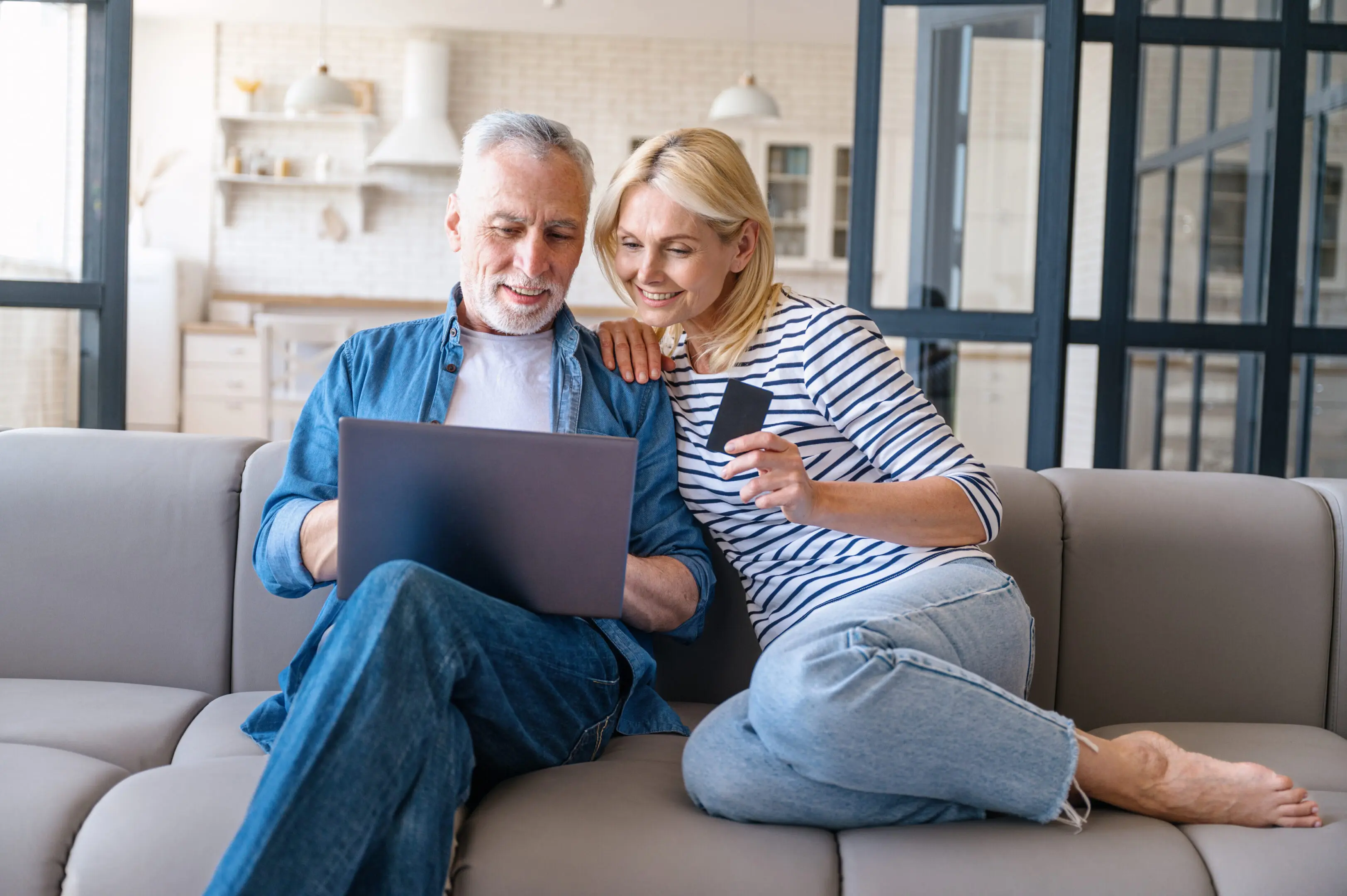 A man and woman sitting on the couch looking at a laptop.
