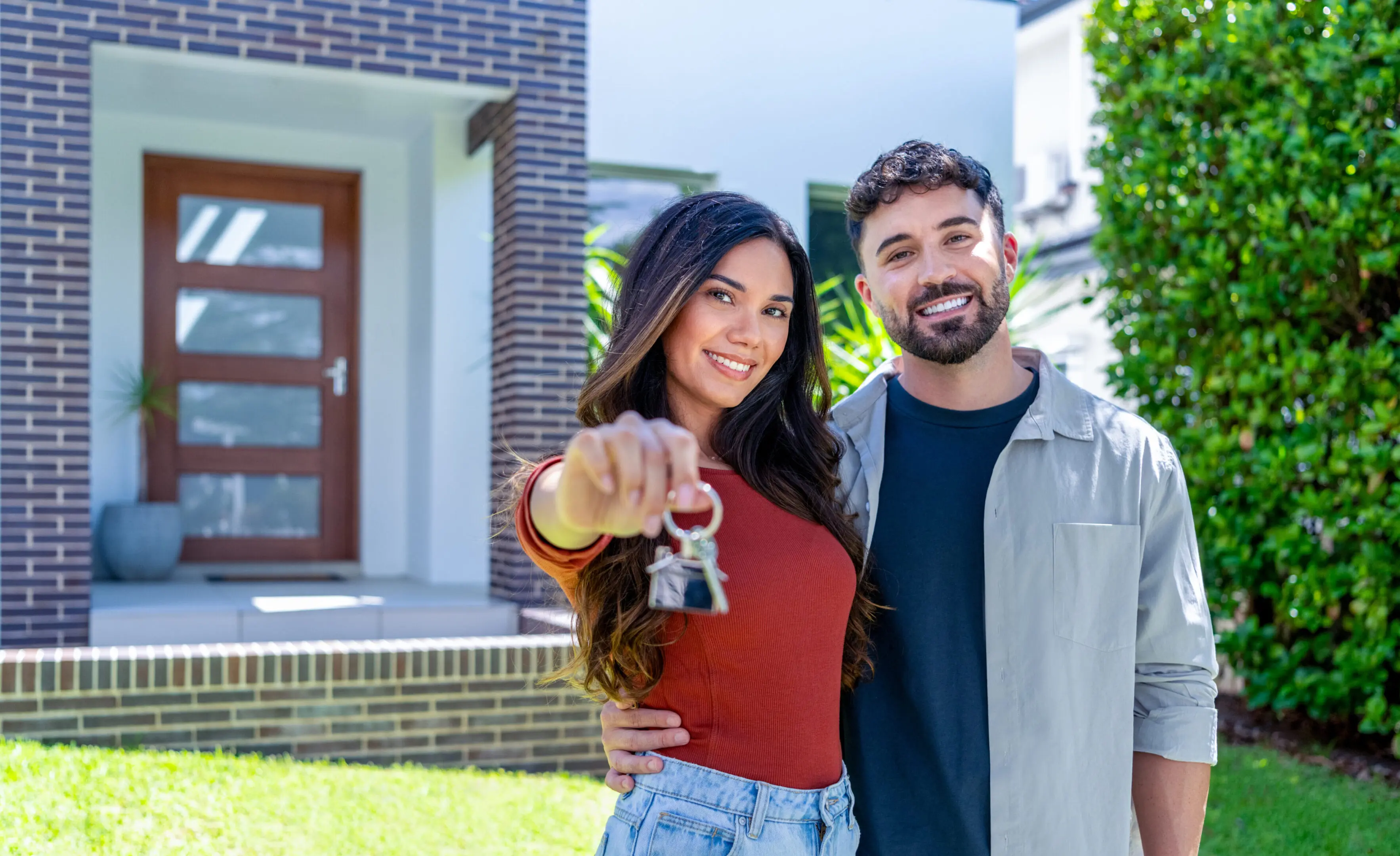 happy woman and man, holding keys from new first house, young family celebrating moving day, happy woman and man, holding keys from new first house, young family celebrating moving day, satisfied customers couple purchase real estate, mortgage and relocation concept. The building can be seen in the background
