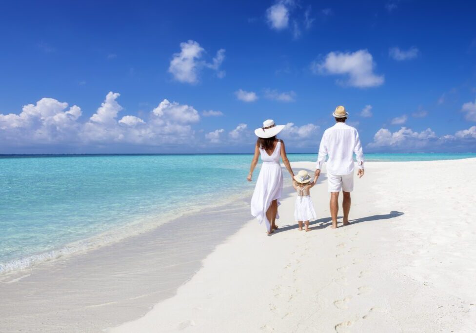 A beautiful family walks together on a tropical paradise beach in the Maldives with turquoise ocean and white sand during their vacation time